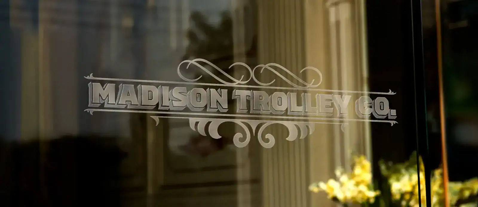 Vintage storefront window with Madison Trolley Co logo, reflecting a cozy, historic ambiance.
