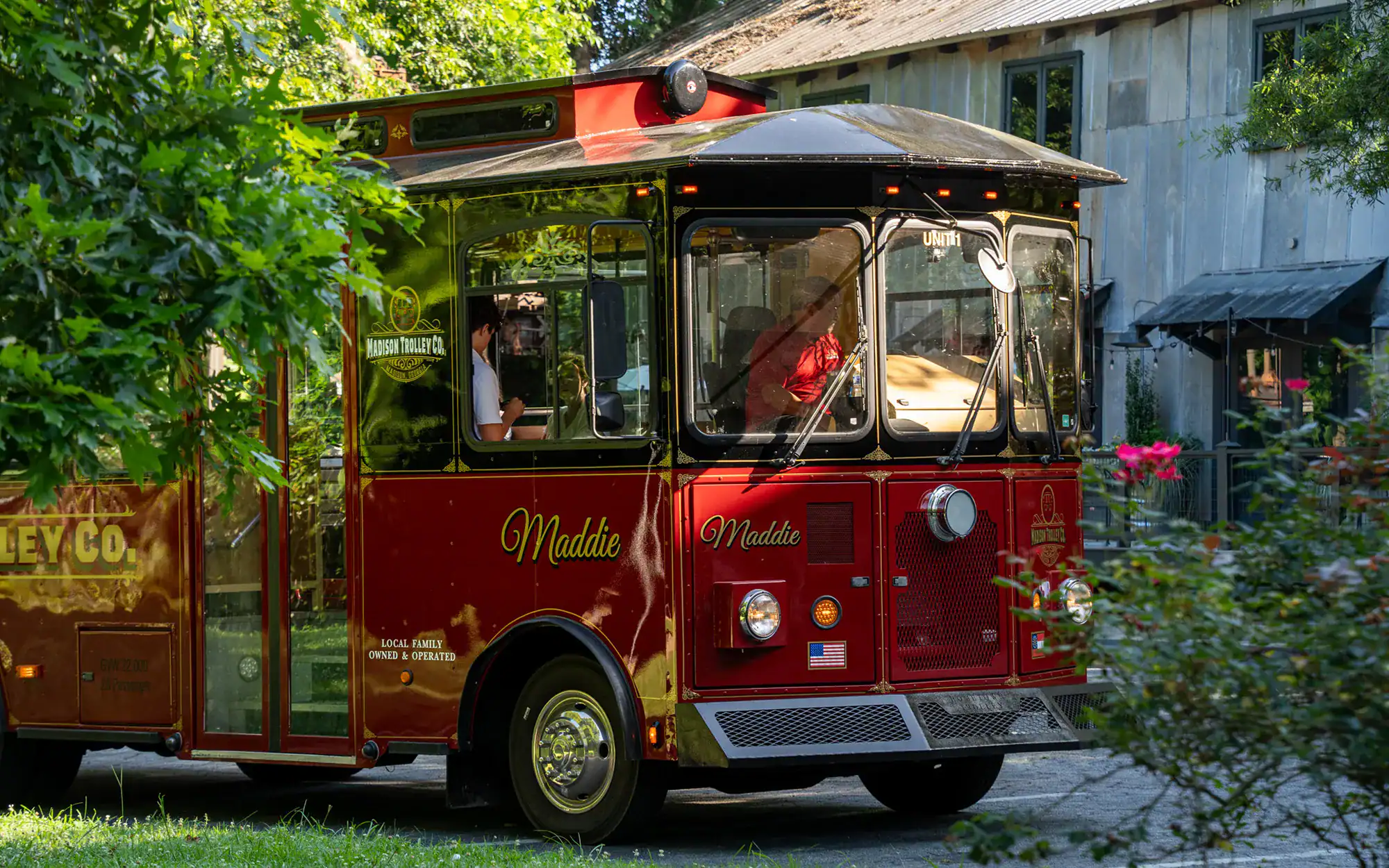 Vintage red Madson Trolley Co. electric bus parked in a lush green setting.