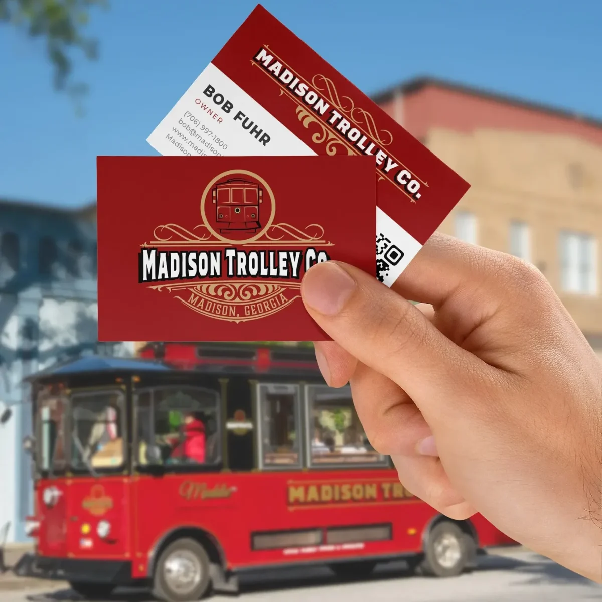 Madison Trolley Co business card held outdoors in front of a red trolley bus.
